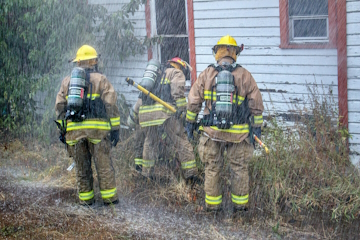 Three fire fighters standing outside of a house with their tools and equipment.