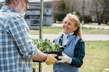 A woman smiling while being handed a pot of plants.